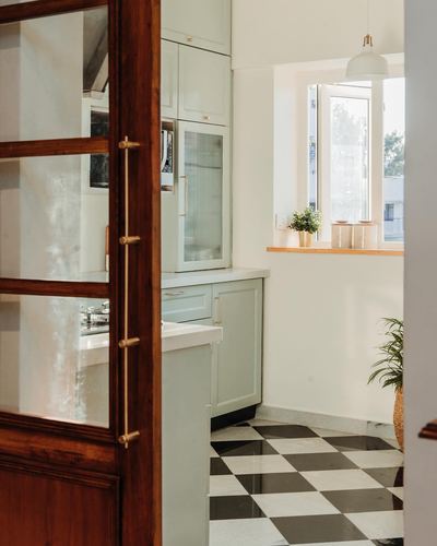 Sage green kitchen seen through a wood-and-glass door with black and white checkerboard floor