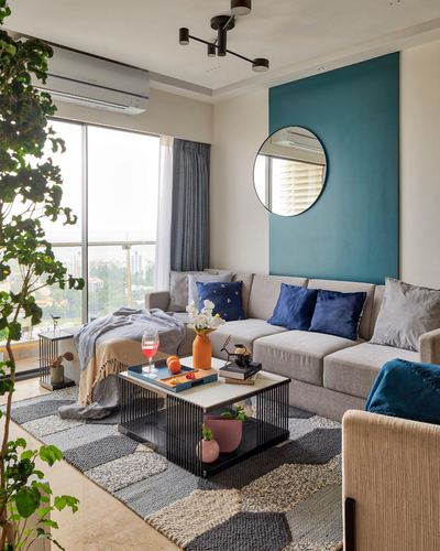 Living room with teal accent wall, round mirror, grey sectional sofa and patchwork rug