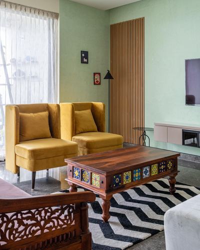 Living room with mustard velvet chairs, carved wood bench, tiled coffee table and sage green walls