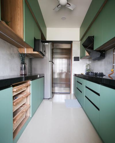 Galley kitchen with sage green cabinets, black countertops, and woven basket storage unit