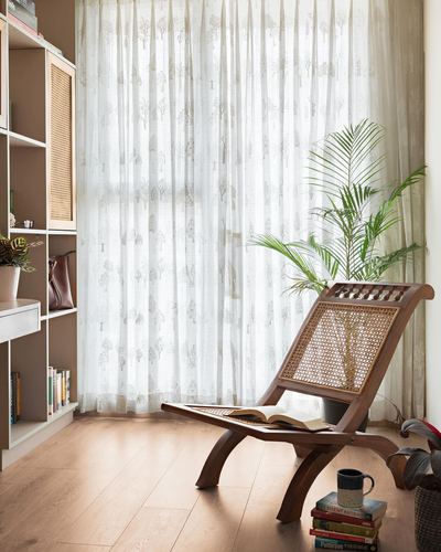 Cane and wood planter's chair with open book by a sheer-curtained window, plant beside it