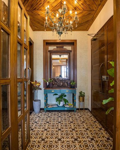 Foyer passage with wood-clad angled ceiling, chandelier, mirror over teal console, and patterned floor tile