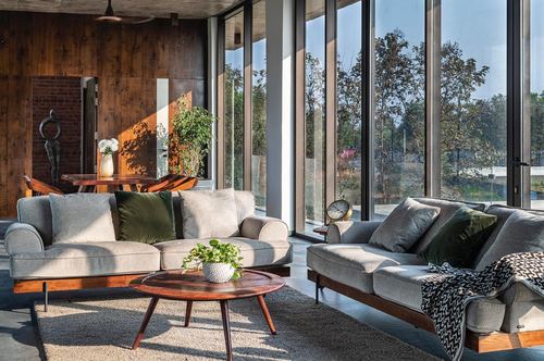Living room with grey sofas and round wood table facing floor-to-ceiling glass wall onto garden