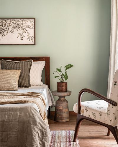 Sage green bedroom with wooden bed, floral armchair, and turned side table with plant