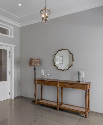 Foyer with wooden console table, cane shelf, scalloped mirror, and lantern pendant light