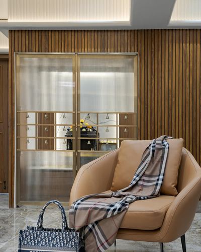 Tan leather armchair with checkered throw in front of a brass-framed glass pooja door, wood-panelled wall