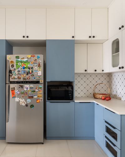 Blue and white kitchen cabinetry with fridge covered in travel magnets and woven basket on counter