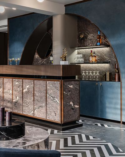 Art deco home bar with arched stone niche, blue cabinetry, and marble-front counter