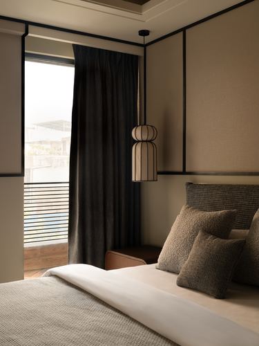 Bedroom corner with textured headboard, layered pillows, and a lantern-style pendant light near a curtained window