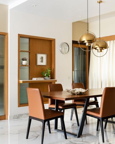 Dining room with wood table, tan leather chairs, marble floor, and brass globe pendant lights