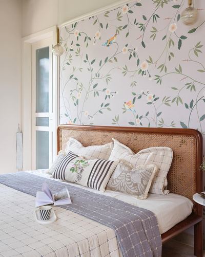Bedroom with cane headboard, floral wallpaper, and layered cushions on a quilted bed
