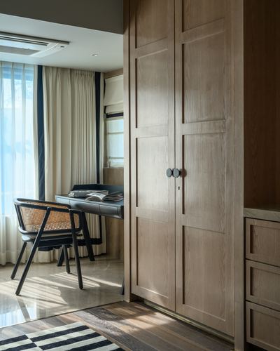 View through a wooden wardrobe doorway into a study with cane chair and desk by window