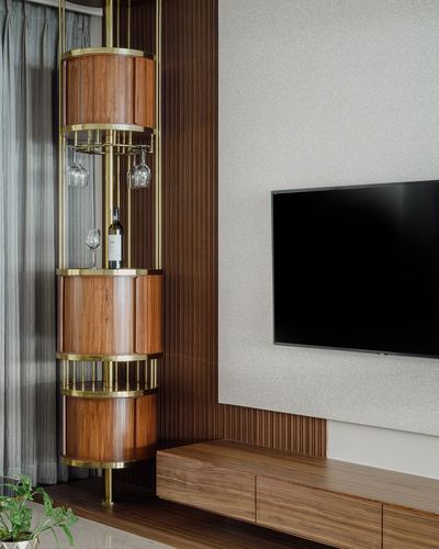 Cylindrical wooden bar cabinet with brass rings beside a TV wall in a living room.