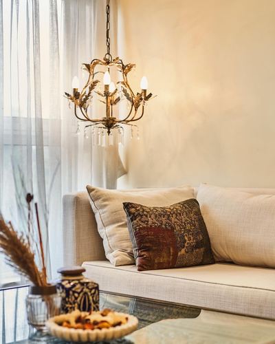 Cream sofa with patterned cushion beneath a brass chandelier near sheer-curtained window
