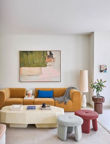 Living room with mustard sofa, abstract painting, carved coffee table and colorful boucle stools
