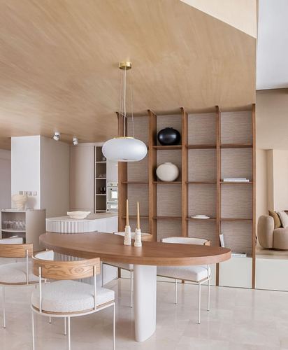 Oval wood dining table with boucle chairs beneath a pendant light in a neutral open-plan home