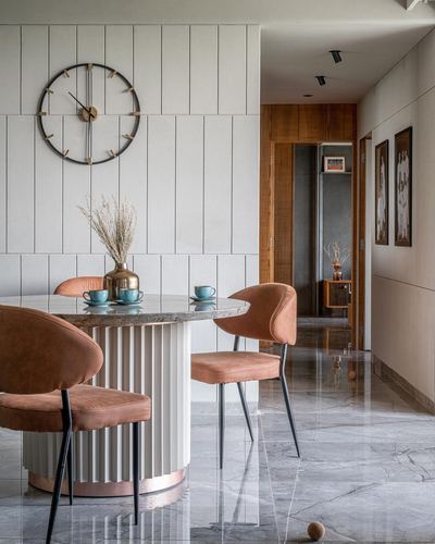Dining nook with round marble table, terracotta chairs, and a large wall clock, opening to a hallway