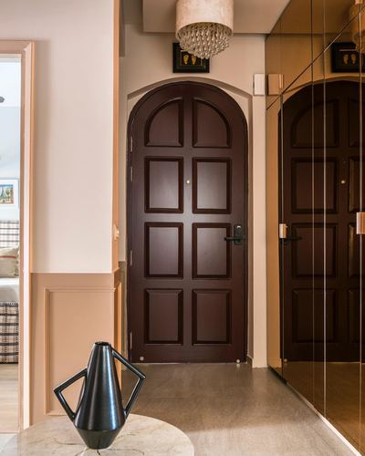 Foyer with arched dark wood door, pendant chandelier, and marble side table holding a black vase