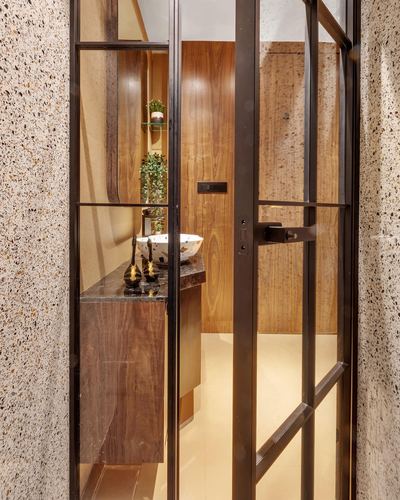 View through a black steel-framed glass door into a wood-panelled powder room with vessel sink