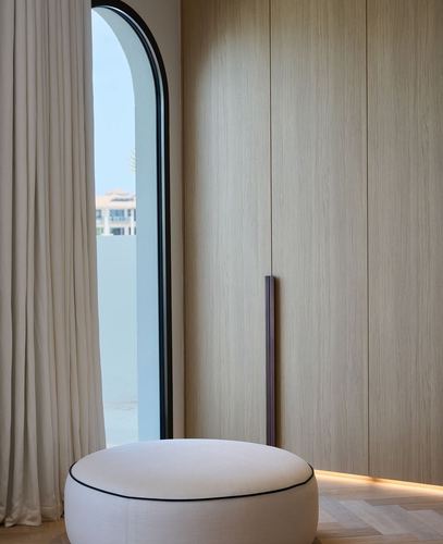 Round white pouf beside arched window and floor-to-ceiling wood wardrobe in a Dubai bedroom