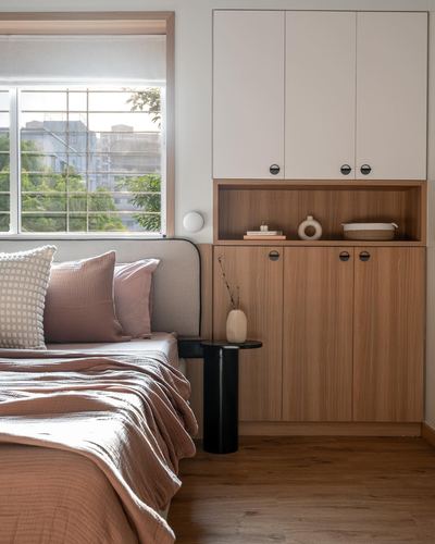 Bedroom corner with curved upholstered headboard, wood cabinetry, and window showing city greenery.
