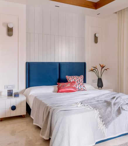 Bedroom with navy velvet headboard, white paneled wall, and layered grey and white bedding