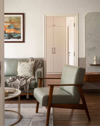Living room with sage green armchair and sofa, wood floor, marble console visible through doorway