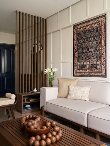 Living room with wood slat screen, arched mirror, and framed tapestry above cream sofa