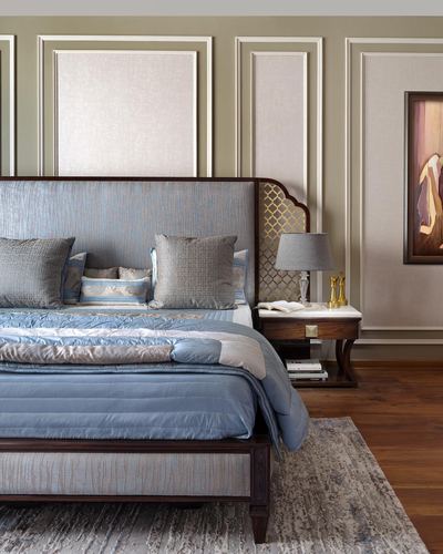Blue upholstered bed with carved wood headboard, cane jali panel, marble-top nightstand and framed art on paneled wall