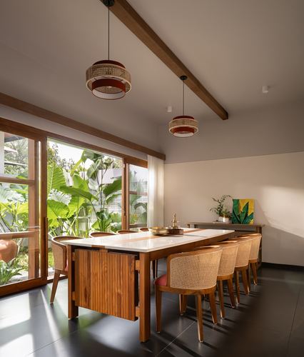 Long wooden dining table with cane chairs beside glass doors opening to a lush garden