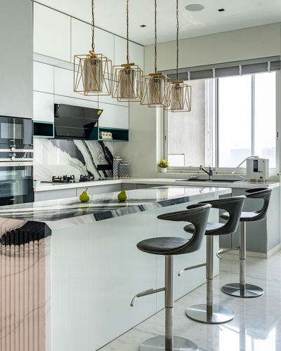 Modern white marble kitchen island with black bar stools under brass geometric pendant lights