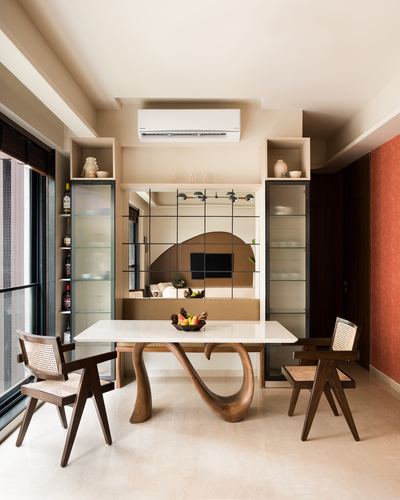 Dining room with sculptural wood-based marble table, cane chairs, fluted glass cabinets, mirrored partition to living room