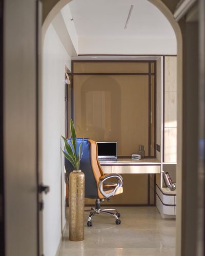 Study nook seen through arched doorway with desk, laptop, leather chair and tall vase