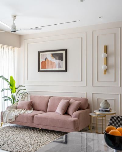 Pink velvet sofa against panelled wall with framed art and brass sconce in Mumbai apartment living room