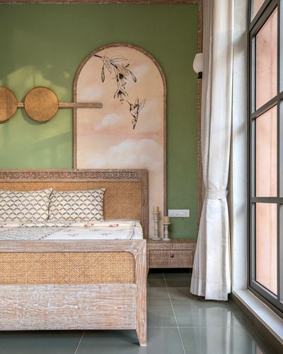 Bedroom with cane bed against green wall, arched hummingbird mural, and large crittall window