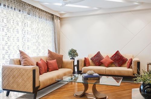 Living room with two tan leather sofas, red cushions, and a glass coffee table by sheer curtained window