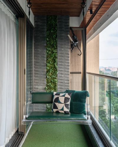 Balcony with hanging green swing bench, vertical garden wall, and city view through glass railing