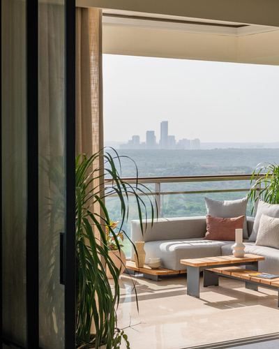Balcony lounge with grey sofa and wooden table framed by sliding glass doors overlooking hazy skyline