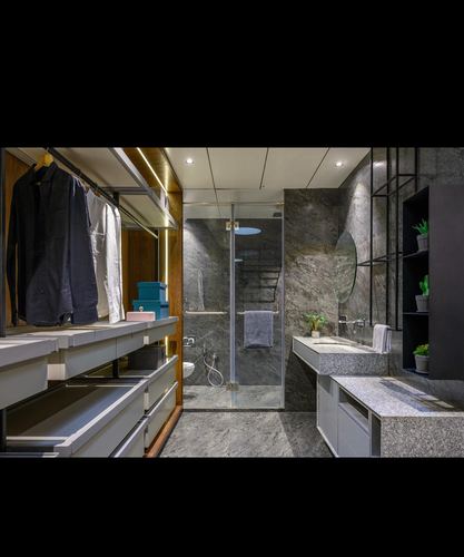 Open wardrobe leading into a stone-clad bathroom with glass shower and floating sink