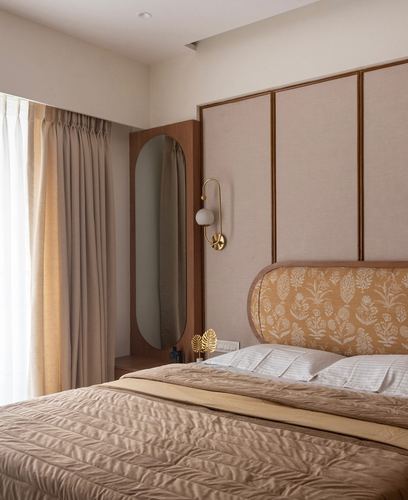 Warm-toned bedroom with paneled headboard wall, oval mirror, and brass sconce beside curtained window
