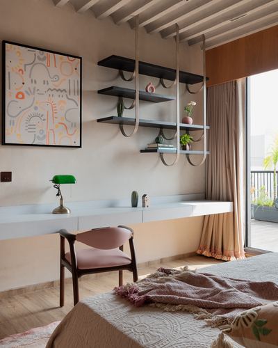 Bedroom study nook with floating desk, looped metal shelving, pink chair and abstract art