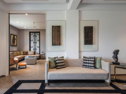 Art deco living room with beige sofa, geometric cushions, framed relic panels and herringbone floor