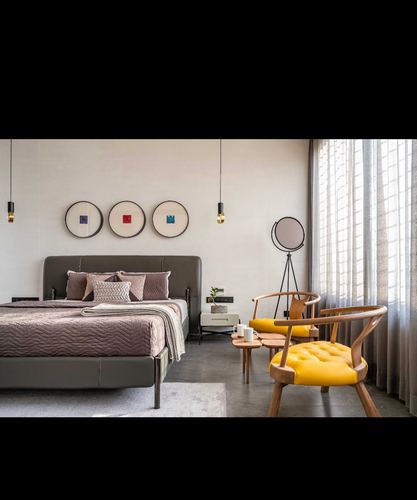 Minimalist bedroom with grey upholstered bed, round wall art, and mustard leather wishbone chairs by window