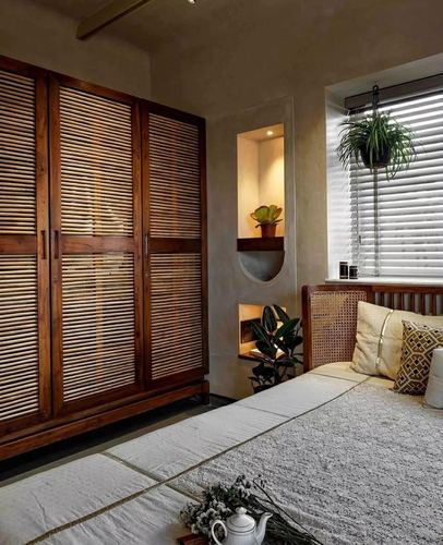 Bedroom corner with louvered wooden wardrobe, lit wall niche, cane headboard bed and hanging plant by window