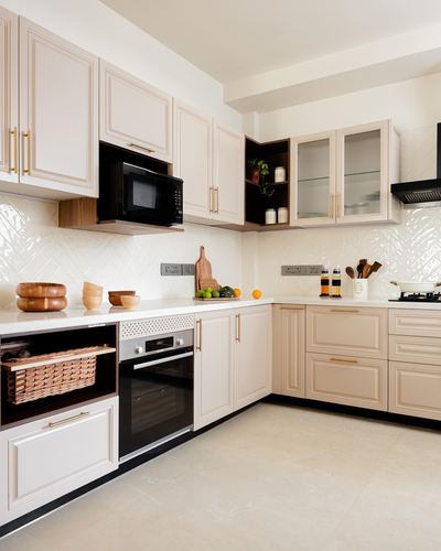 Cream L-shaped kitchen with paneled cabinetry, brass handles, and herringbone tile backsplash