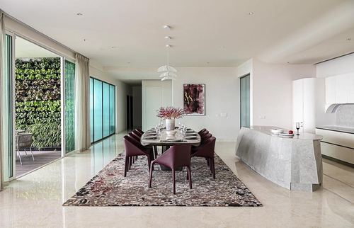 Open-plan dining area with marble floor, burgundy leather chairs, and a living wall visible through glass doors