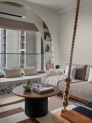 Living room with arched window seat, niche shelving, sofa, round wood coffee table and hanging swing rope