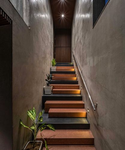 Narrow staircase with terracotta treads, black risers, potted plants, lit by recessed lights