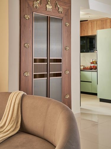 Wood-framed fluted glass door with brass lotus motifs beside sofa, kitchen visible beyond