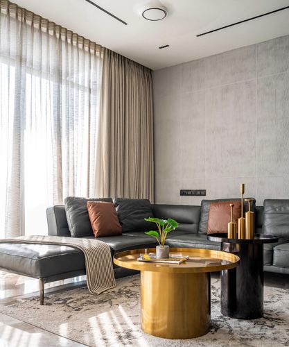 Charcoal leather sectional sofa with brass round coffee table against textured stone wall